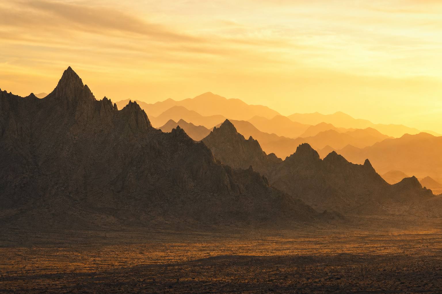 A jagged desert ridgeline silhouetted against a golden sunset sky, rising and falling like the line of an elevation profile